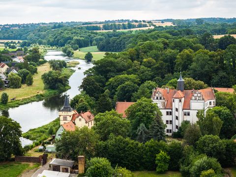 Vogelperspektive auf das Wasserschloss Podenwitz, umgeben von Bäumen und grüner Landschaft, mit Blick auf die Mulde.
