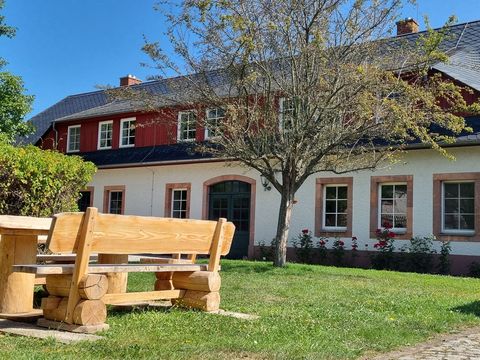 Außenansicht des Jugendbegegnungszentrums Seelitz mit Innenhof, heller Gebäudefassade und einer Holzsitzgarnitur in der Mitte, umgeben von Rasen und Pflanzen bei sonnigem Wetter.