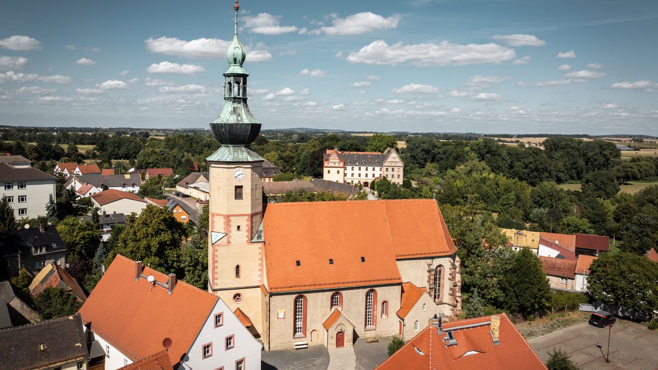 Eine Luftaufnahme zeigt die Kirche in Trebsen mit ihrem markanten Turm und dem umliegenden Gebäuden.