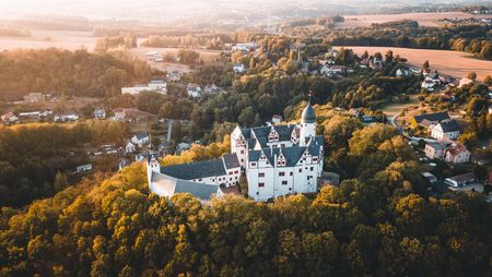 Eine atmosphärische Drohnenaufnahme von Schloss Rochsburg, umgeben von Wald.