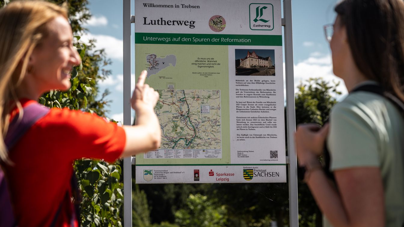 Das Bild zeigt zwei Wanderinnen, die an einer Infotafel zum Lutherweg Sachsen stehen.