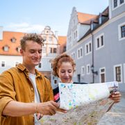 Zwei Tourist:innen im Schlosskomplex Glauchau, eine Person hält eine Übersichtskarte, sie laufen durch die historischen Wege.