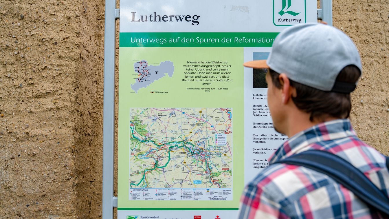 Ein Wanderer steht vor einem Wegweiser des Lutherweg Sachsens.