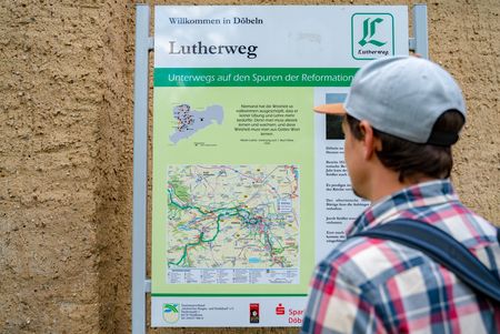 Ein Wanderer steht vor einem Wegweiser des Lutherweg Sachsens.