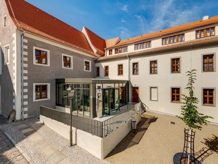 Blick auf ein modernes Gebäude mit grau-weißer Fassade und verglastem Eingang im Innenhof.