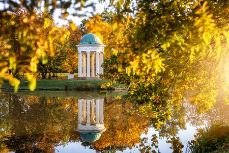 Das Bild zeigt den weißen Pavillion am Teich in der Herbstsonne. Im ganzen Park liegen schon gelbe Blätter.