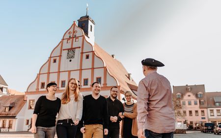 Eine Gruppe Touristen und ein Stadtführer mit Kochhaube vor dem Grimmaer Rathaus.