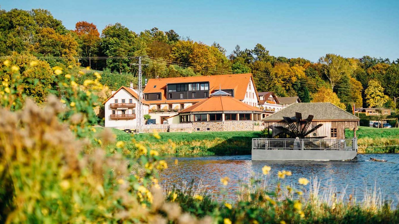 Das Bild zeigt die Anlage des Hotels Zur Schiffsmühle in Grimma hinter dem Flusslauf der Mulde.